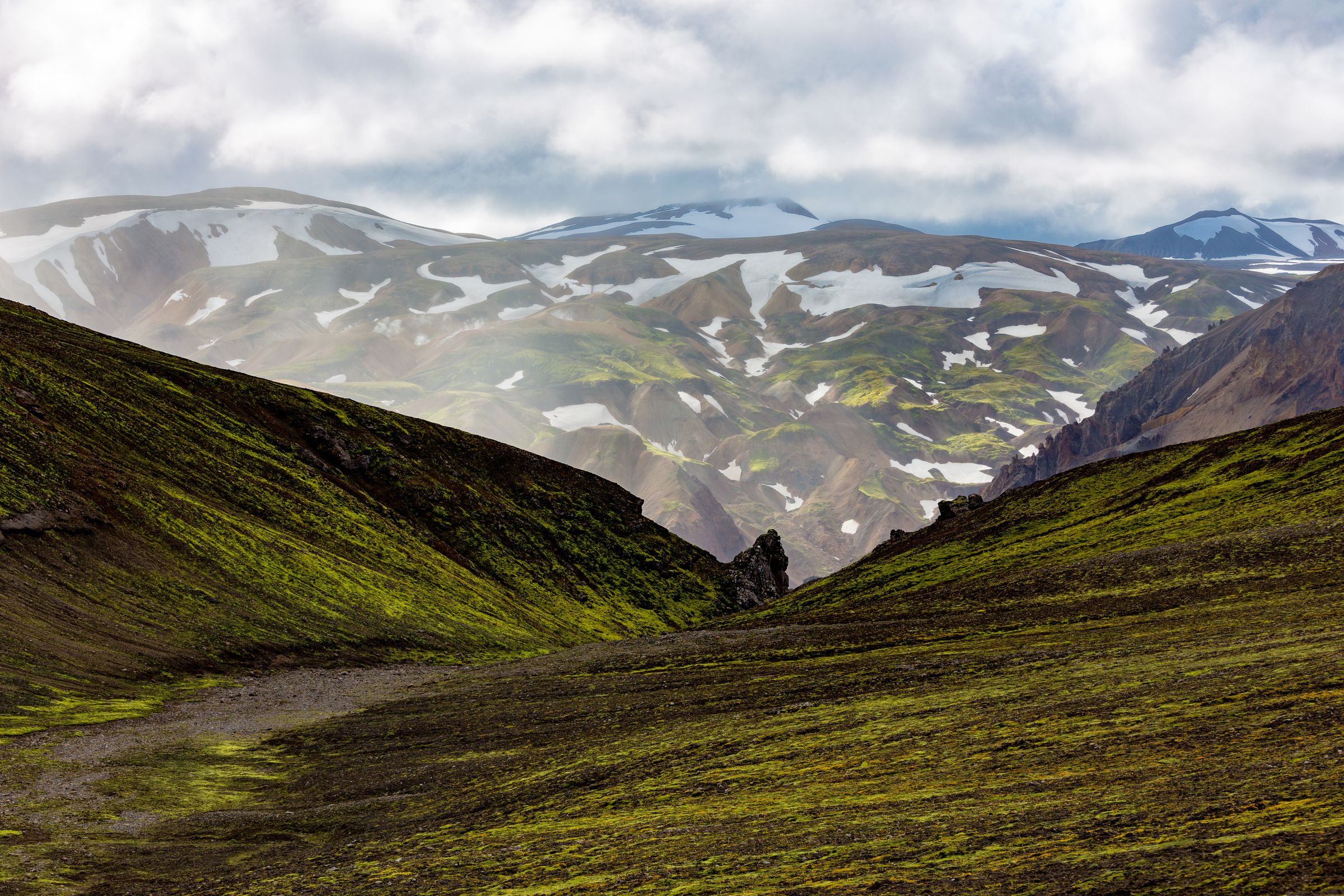 Sudurnamur valley surrounded by mountains covered in snow on a cloudy day .
