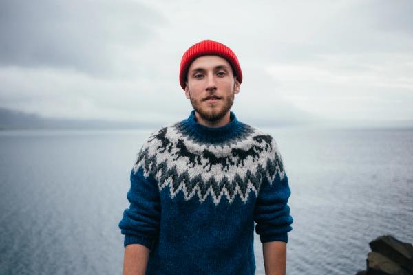 a man wearing a blue sweater and a red hat is standing in front of a body of water .