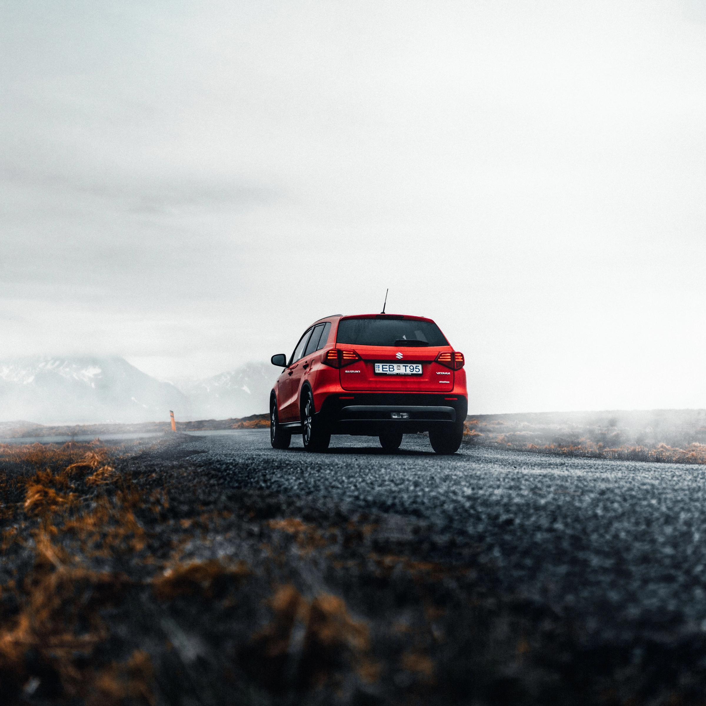 Red SUV on a misty road with distant mountains.