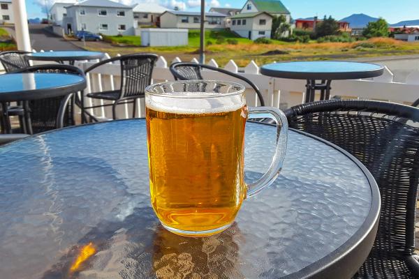 A mug of beer on a glass table at an outdoor cafe with houses in the background.