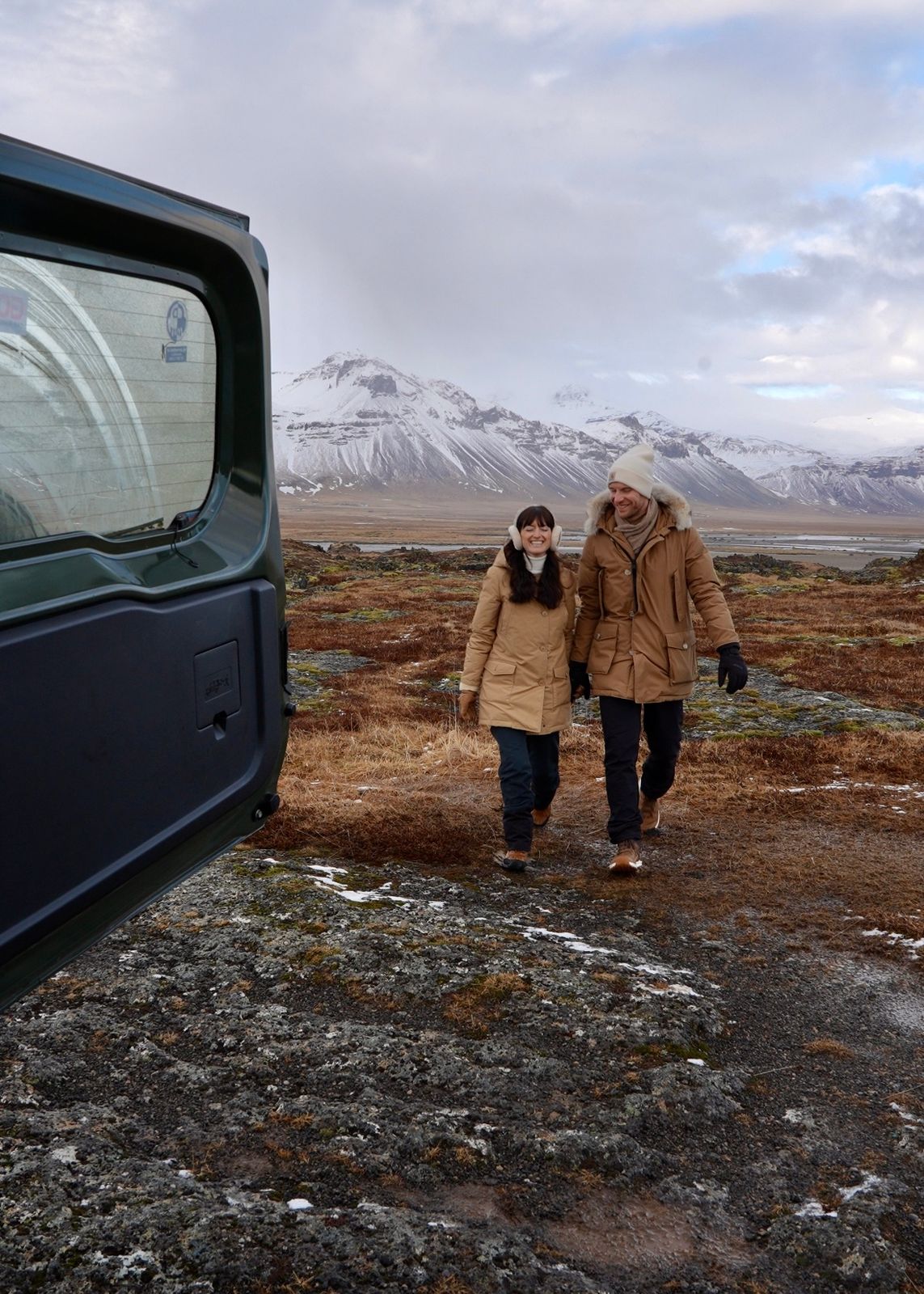 a man and woman are walking in a field with mountains in the background