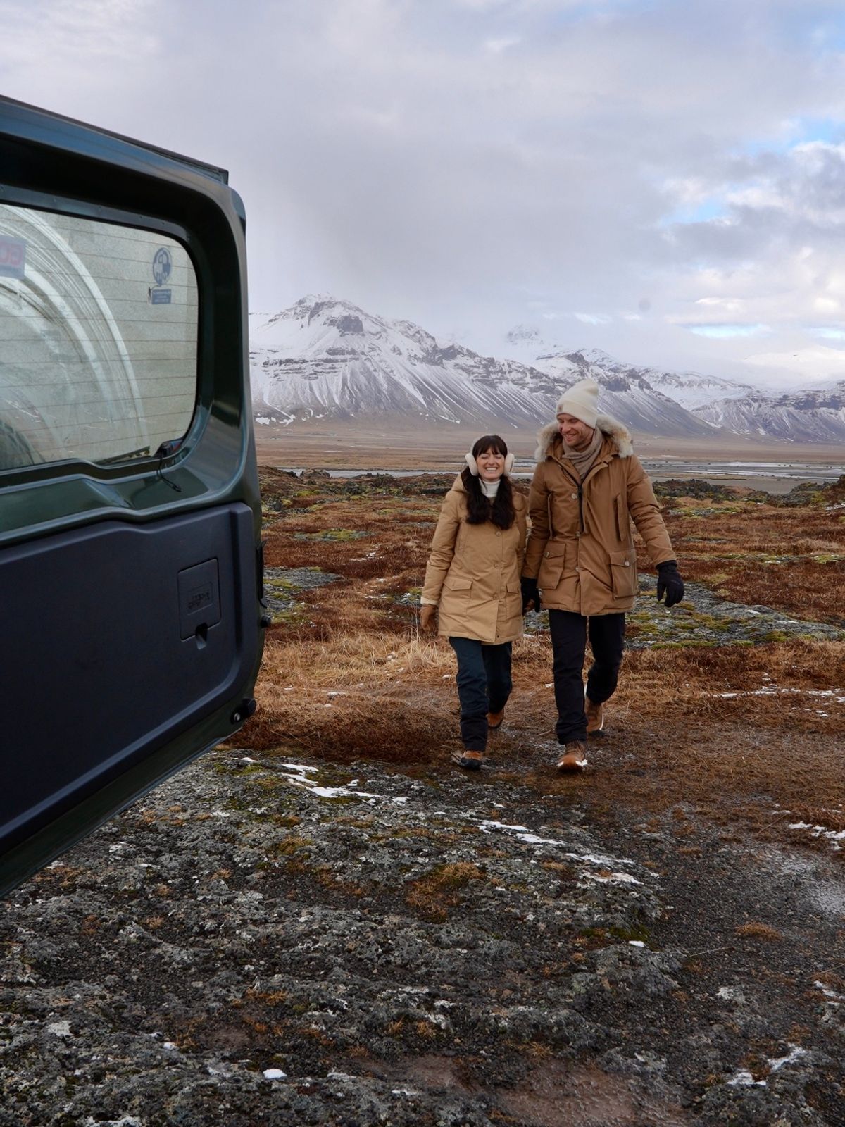 a man and woman are walking in a field with mountains in the background