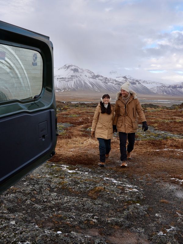a man and woman are walking in a field with mountains in the background