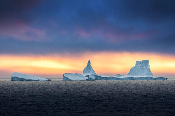 a large iceberg in the middle of the ocean at midnight sun in iceland.