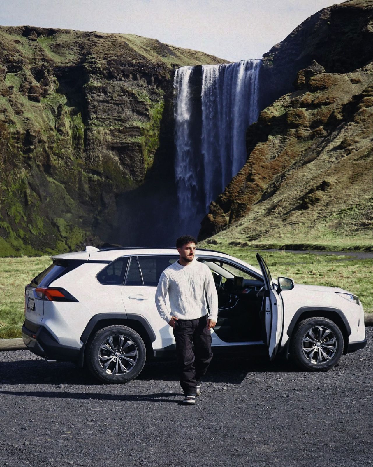a man standing next to a white suv in front of a waterfall