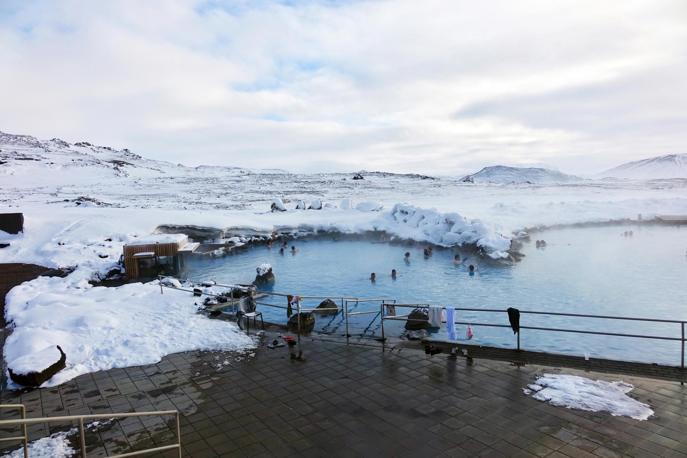 People bathing in a steaming blue geothermal pool surrounded by a snow-covered landscape.