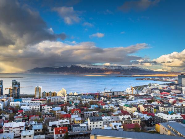 Una ciudad con un montón de edificios al lado del mar, con montañas de fondo y nubes en el cielo
