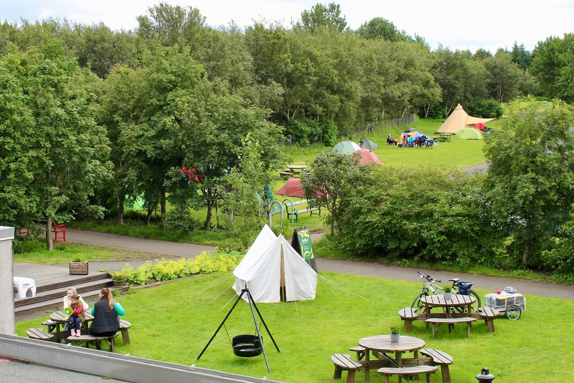 un camping con hierba verde, árboles y mesas de madera para comer