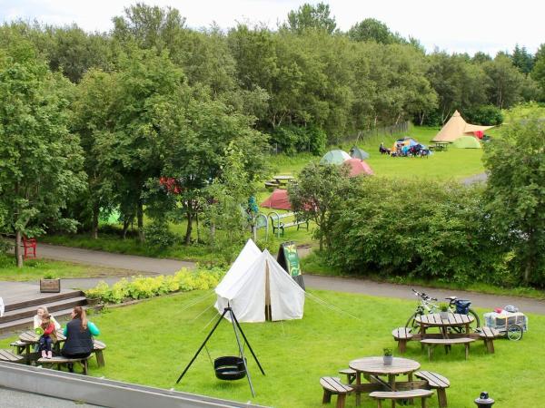 Camping verde con mesas, un columpio y una tienda de campaña blanca