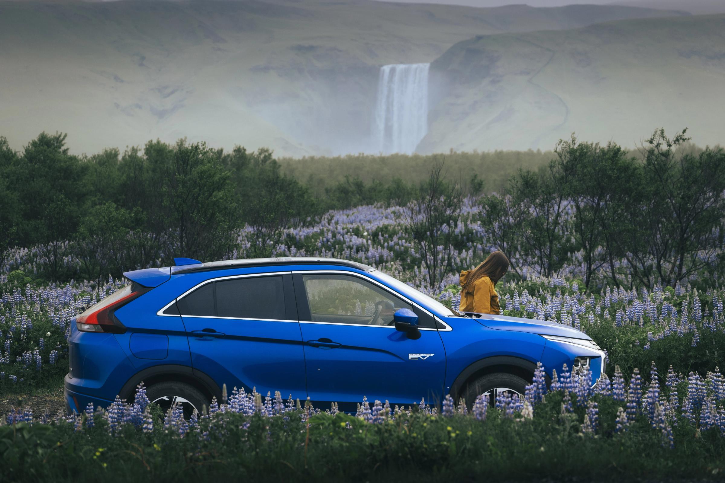 Mitsubishi Eclipse Cross aparcado en un campo de flores, con una cascada y una persona al fondo