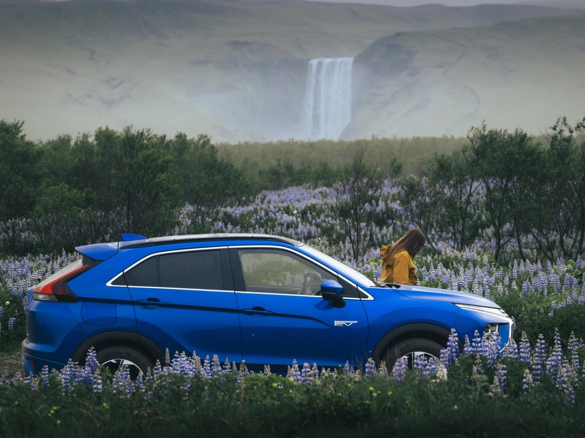 Vista de la cascada con el Mitsubishi Eclipse Cross Mitsubishi Eclipse Cross aparcado en un campo de flores, con una cascada y una persona al fondo