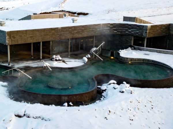 Steaming outdoor thermal pools surrounded by snow and modern buildings.