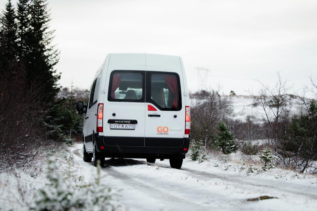 Ein großes Wohnmobil fährt auf einem Weg an hohen Nadelbäumen vorbei, Wohnmobilvermietung Island