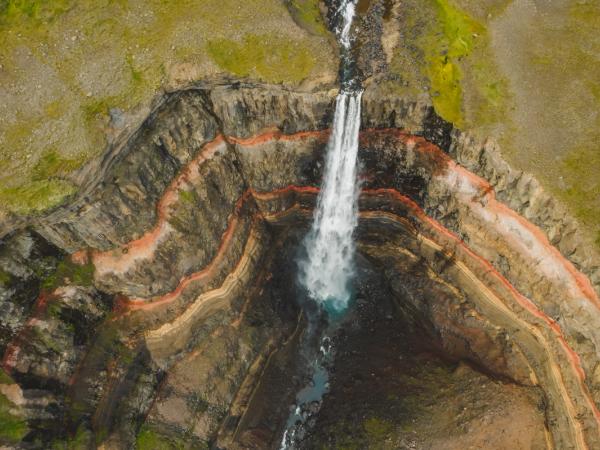 an aerial view of Hengifoss waterfall in the middle of a canyon .