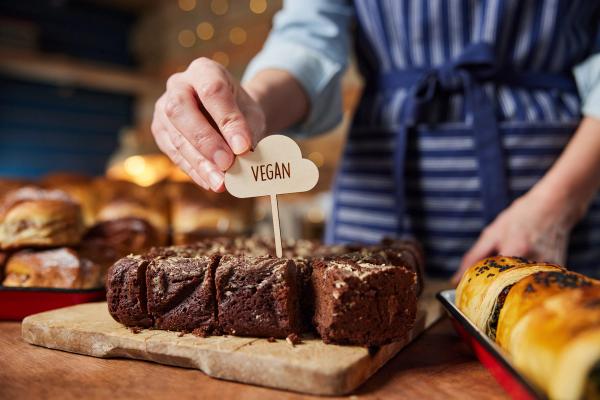 Person placing a "VEGAN" sign into a sliced chocolate cake at a bakery.