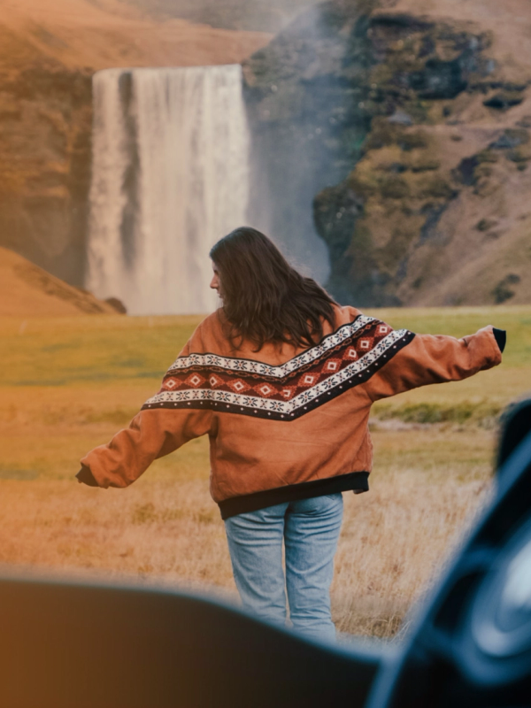 a woman in a sweater stands in front of a waterfall