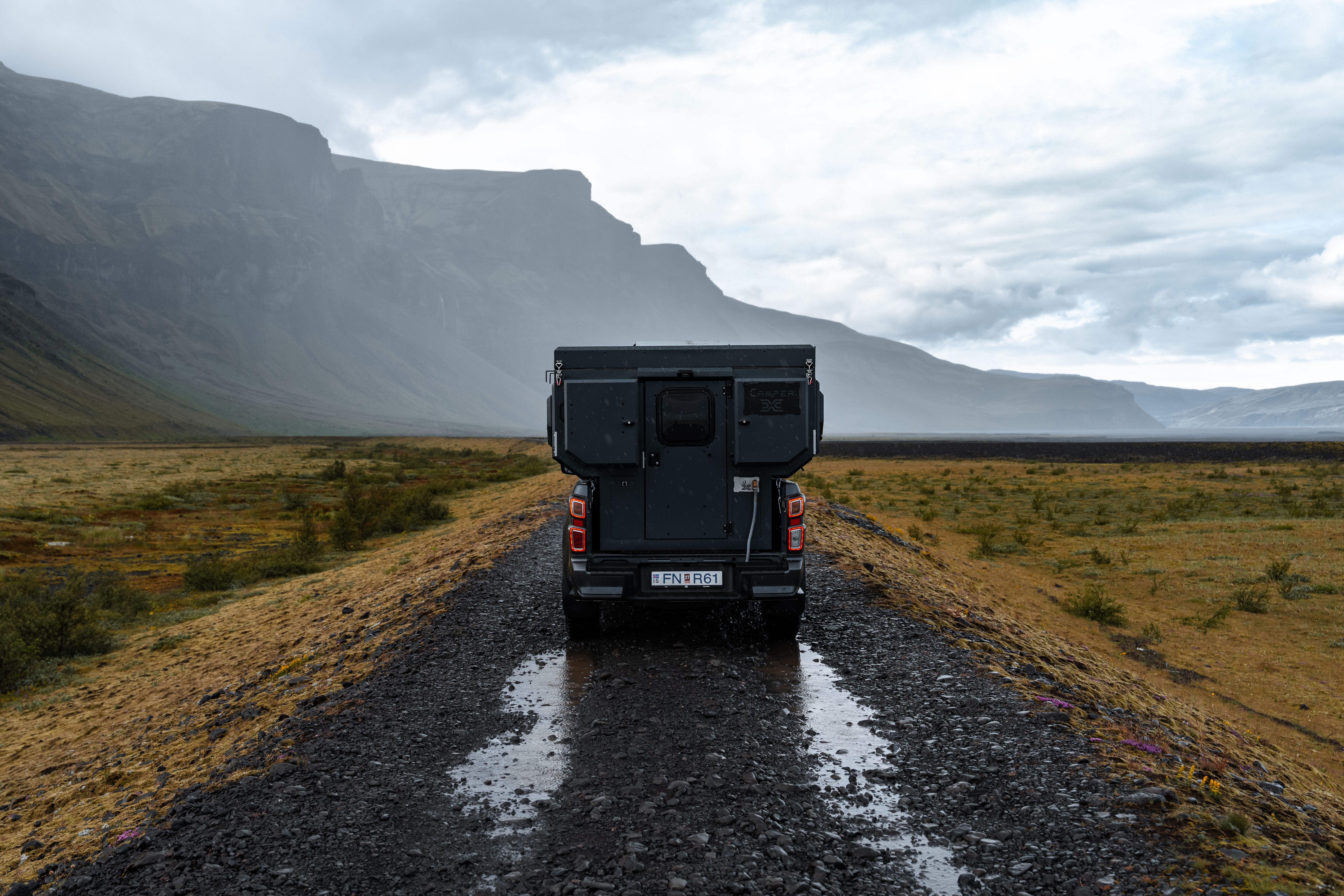 Una autocaravana 4x4 para 2 personas en una carretera de grava rumbo a una montaña, alquiler de autocaravanas en Islandia