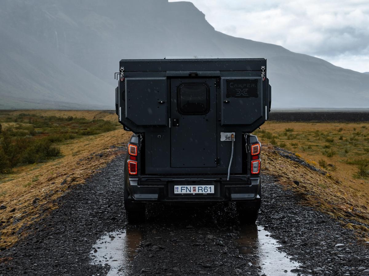 Vista trasera de la autocaravana 4x4 Una autocaravana 4x4 para 2 personas en una carretera de grava rumbo a una montaña, alquiler de autocaravanas en Islandia
