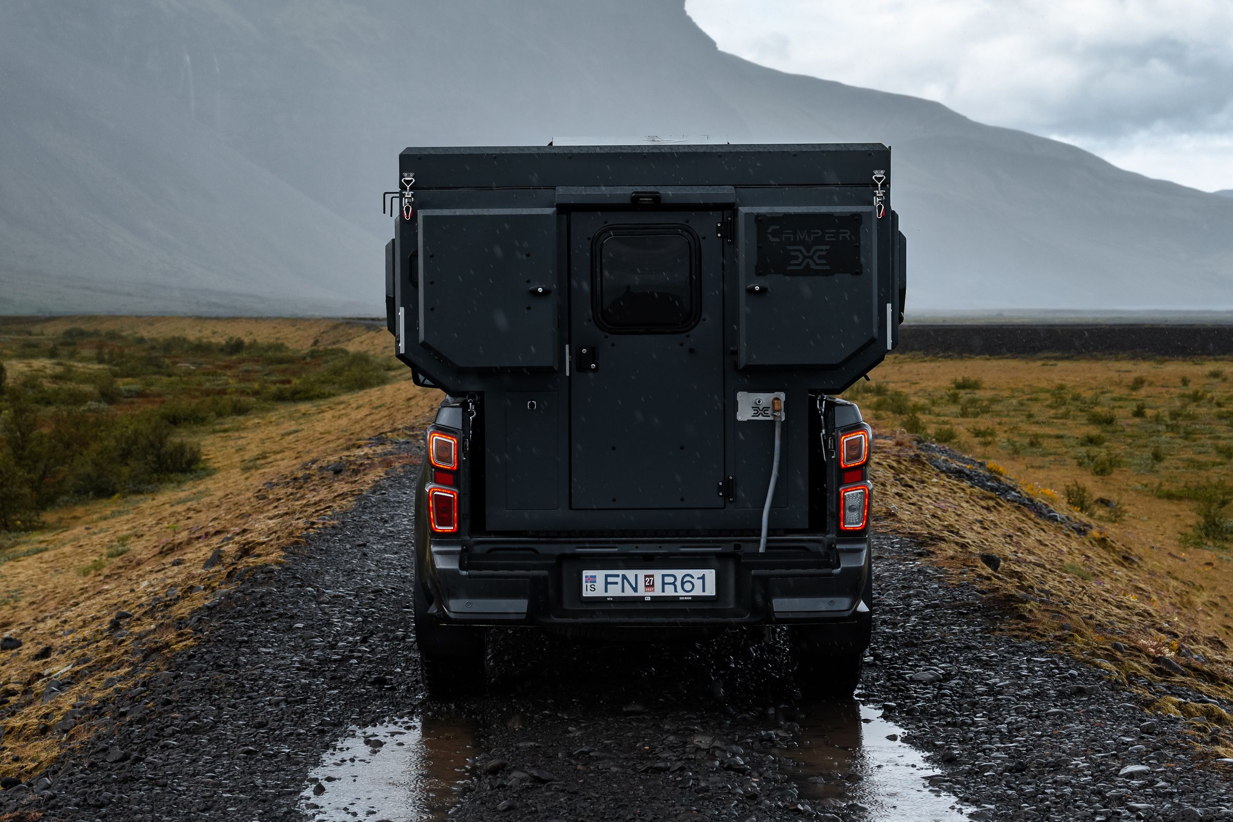 Vista trasera de la autocaravana 4x4 Una autocaravana 4x4 para 2 personas en una carretera de grava rumbo a una montaña, alquiler de autocaravanas en Islandia