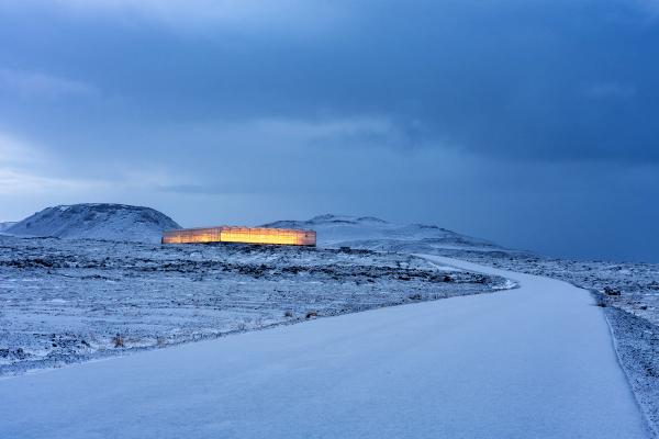 A glowing building in a vast, snowy landscape under a dark sky, with a winding road.