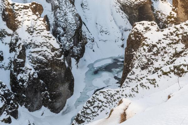 A snow-covered canyon with steep rocky walls and a frozen river at the bottom.