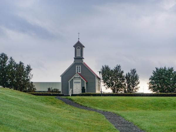 a small church with a red roof is sitting on top of a grassy hill at Snorrastofa in Reykholt Iceland.