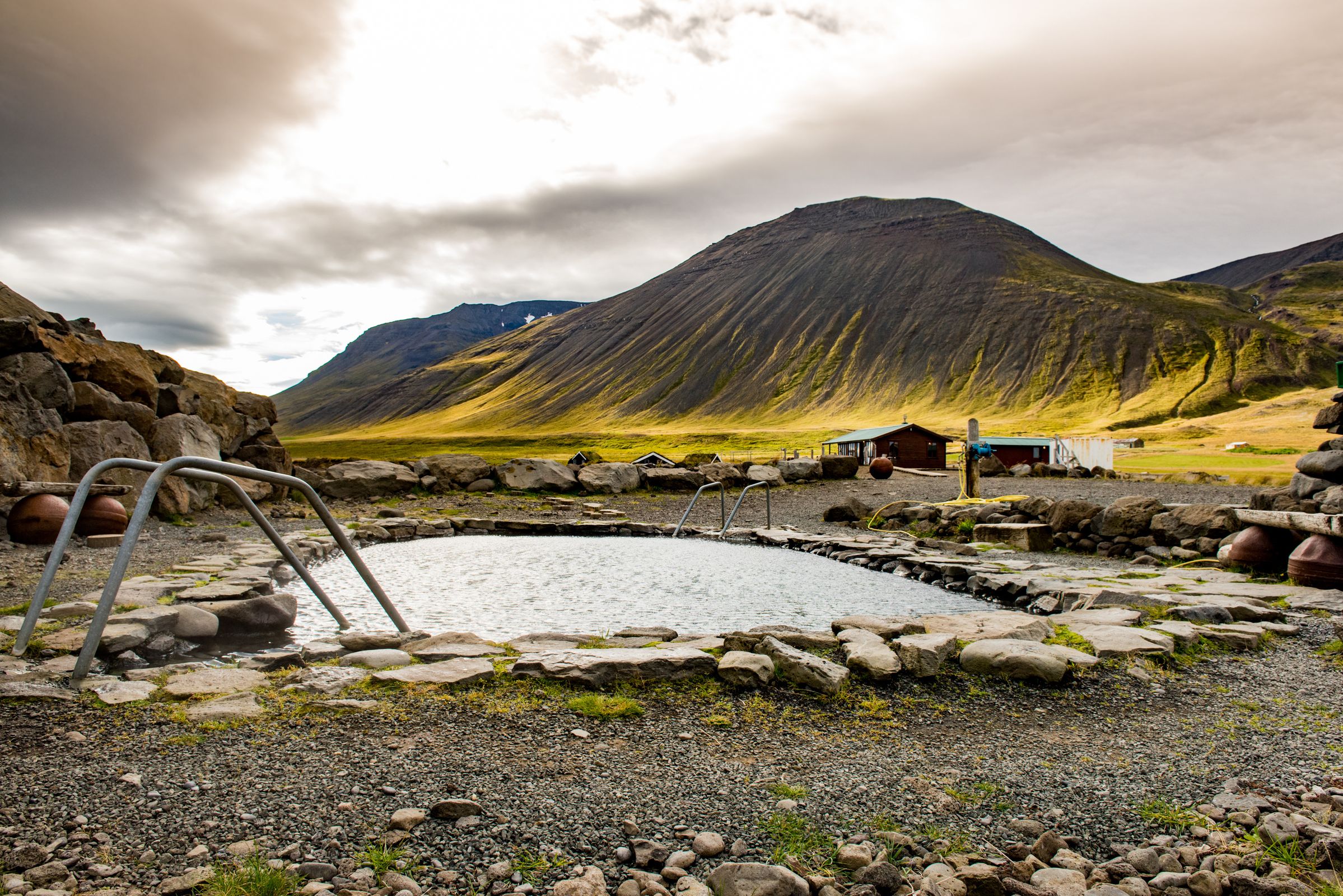 there is a swimming pool in the middle of a rocky area with a mountain in the background at Grettislaug in north iceland.