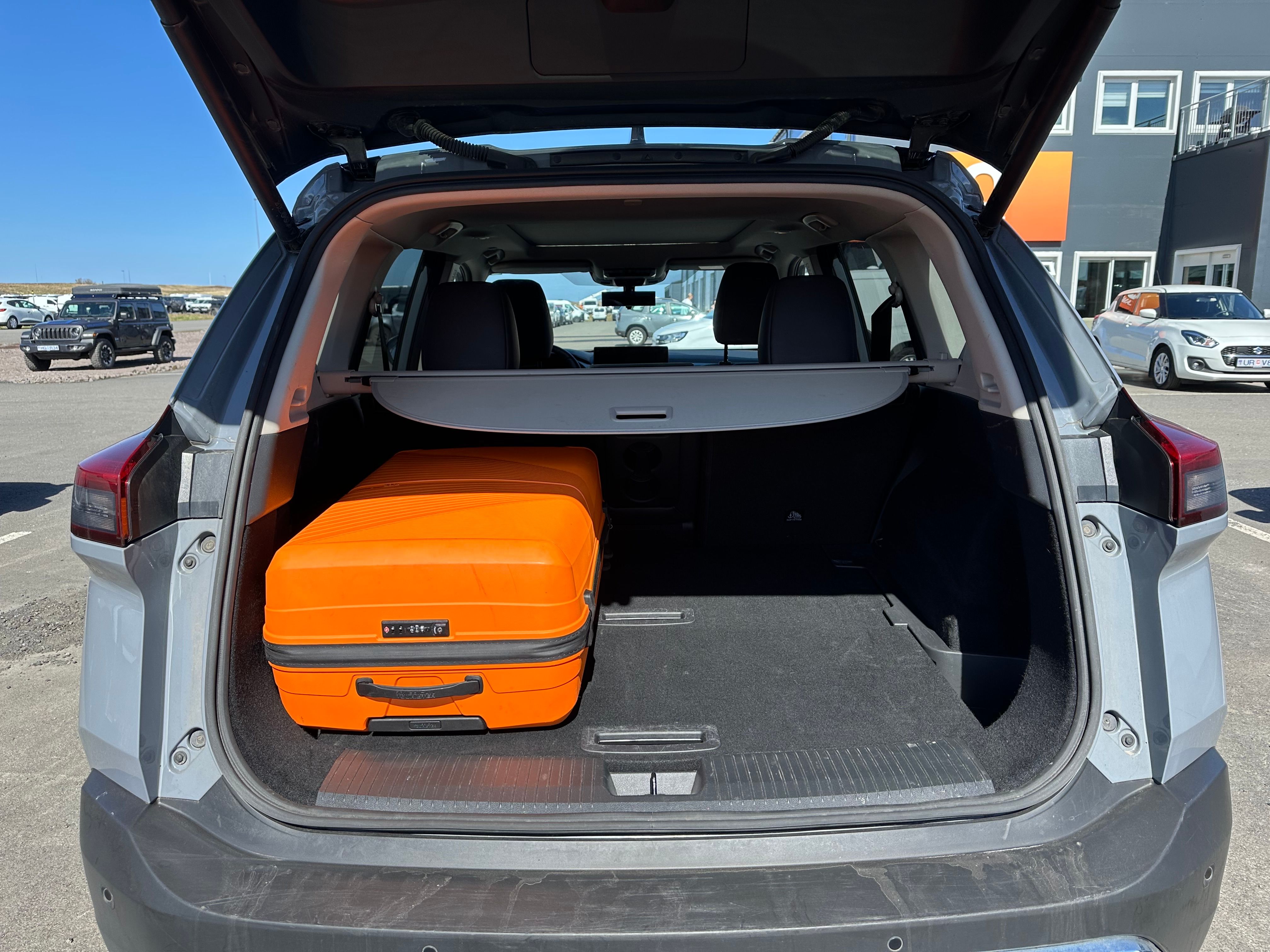The open trunk of a gray SUV with an orange suitcase inside.