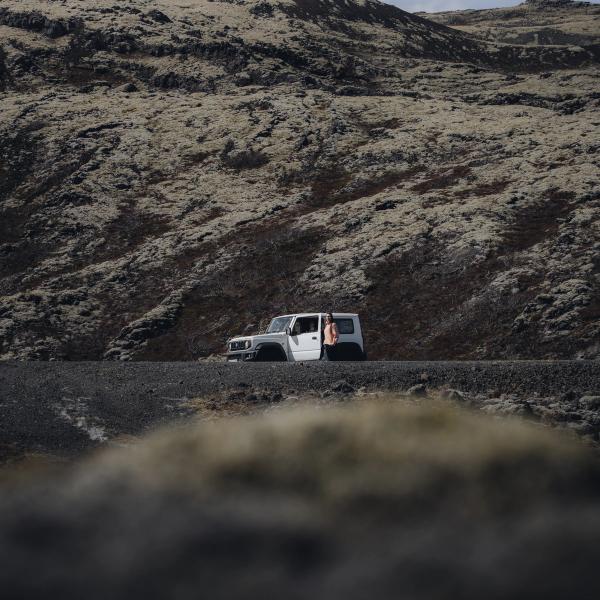 A white SUV with an open driver's door and a person standing next to it, parked on a dark road in a landscape of moss-covered hills.