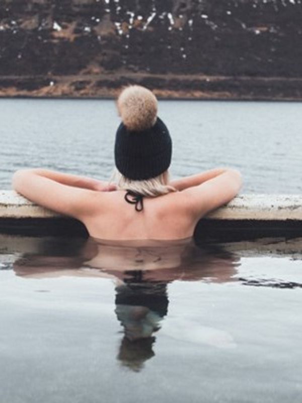 Mujer dentro de un agua termal al lado de un lago