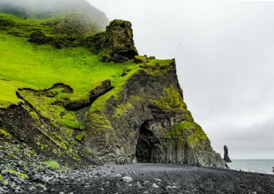 a cave under a cliff on a black sand beach