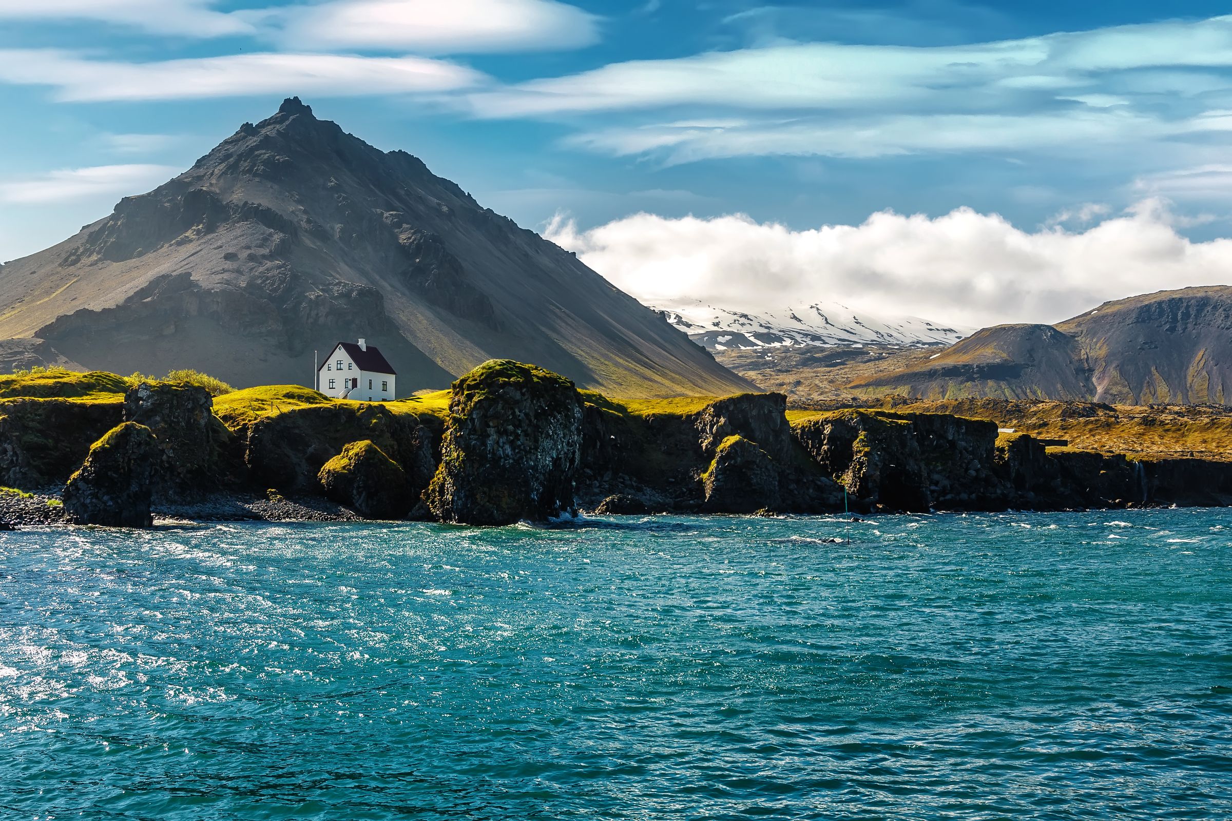 landscape with small cliffs next to the sea a house on top and a mountain on the background