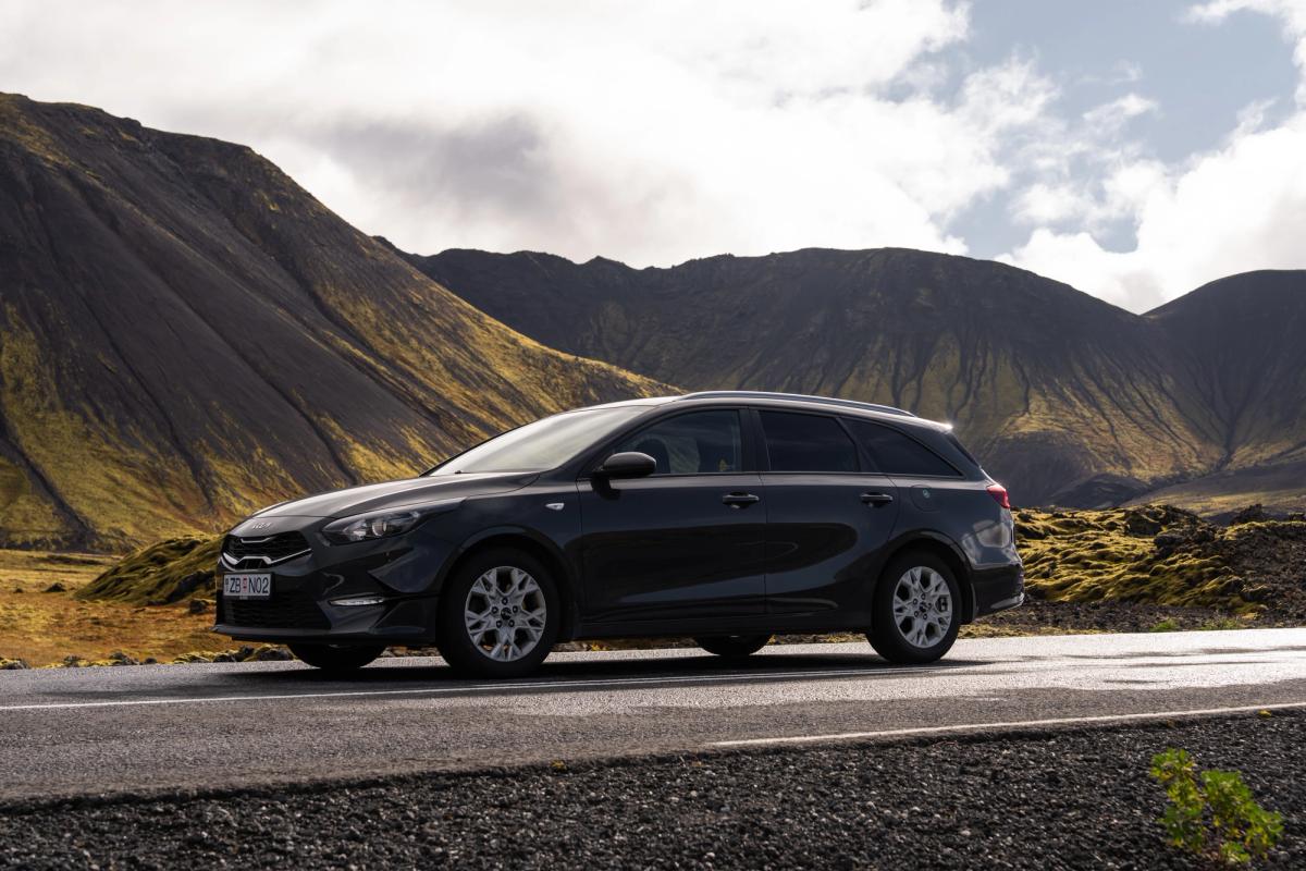 Kia Ceed familiar de alquiler en Islandia, aparcado en una carretera asfaltada al pie de unas montañas cubiertas de musgo