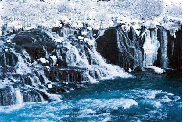 a waterfall is surrounded by snow and rocks in the middle of a river at Hraunfossar in Iceland.