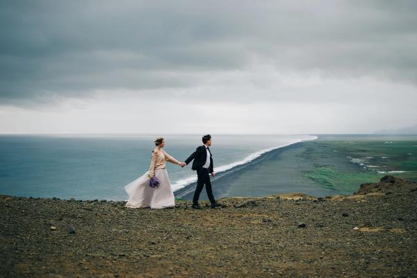 a bride and groom are walking on top of a hill overlooking the ocean .