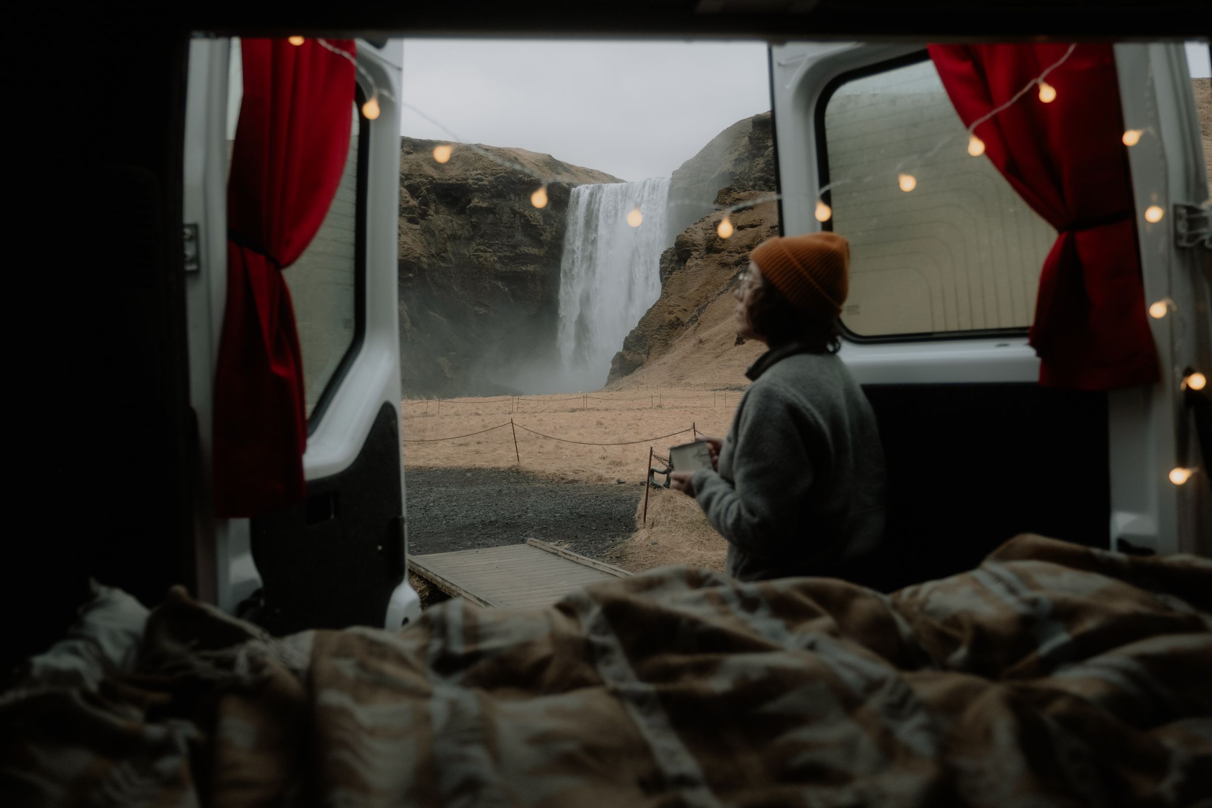a woman is sitting in a van looking out the window at a waterfall .