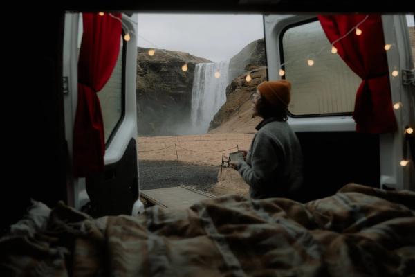 a woman is sitting in a van looking out the window at a waterfall .