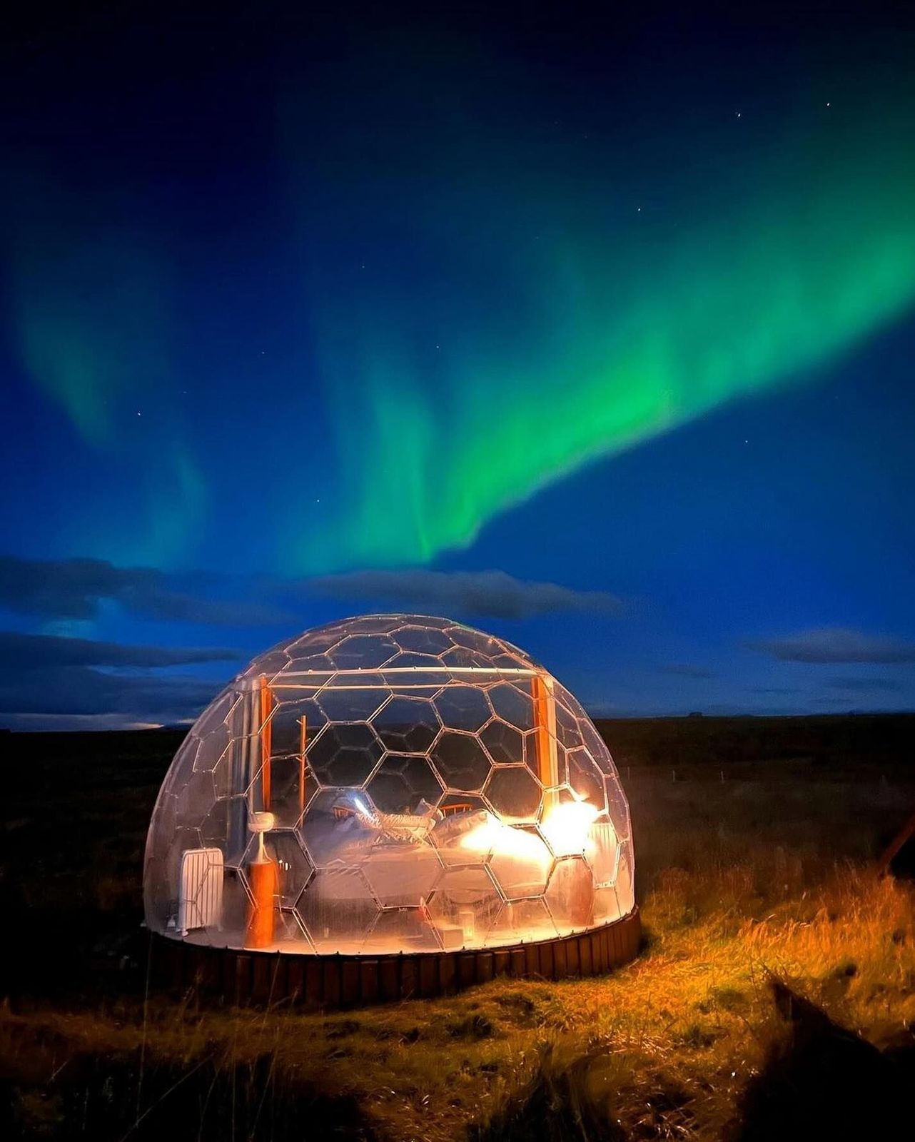 a clear dome with a bed inside of it with the aurora borealis in the background .