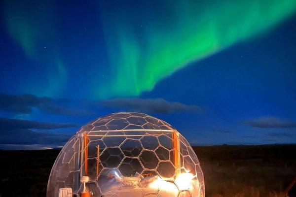 a clear dome with a bed inside of it with the aurora borealis in the background .