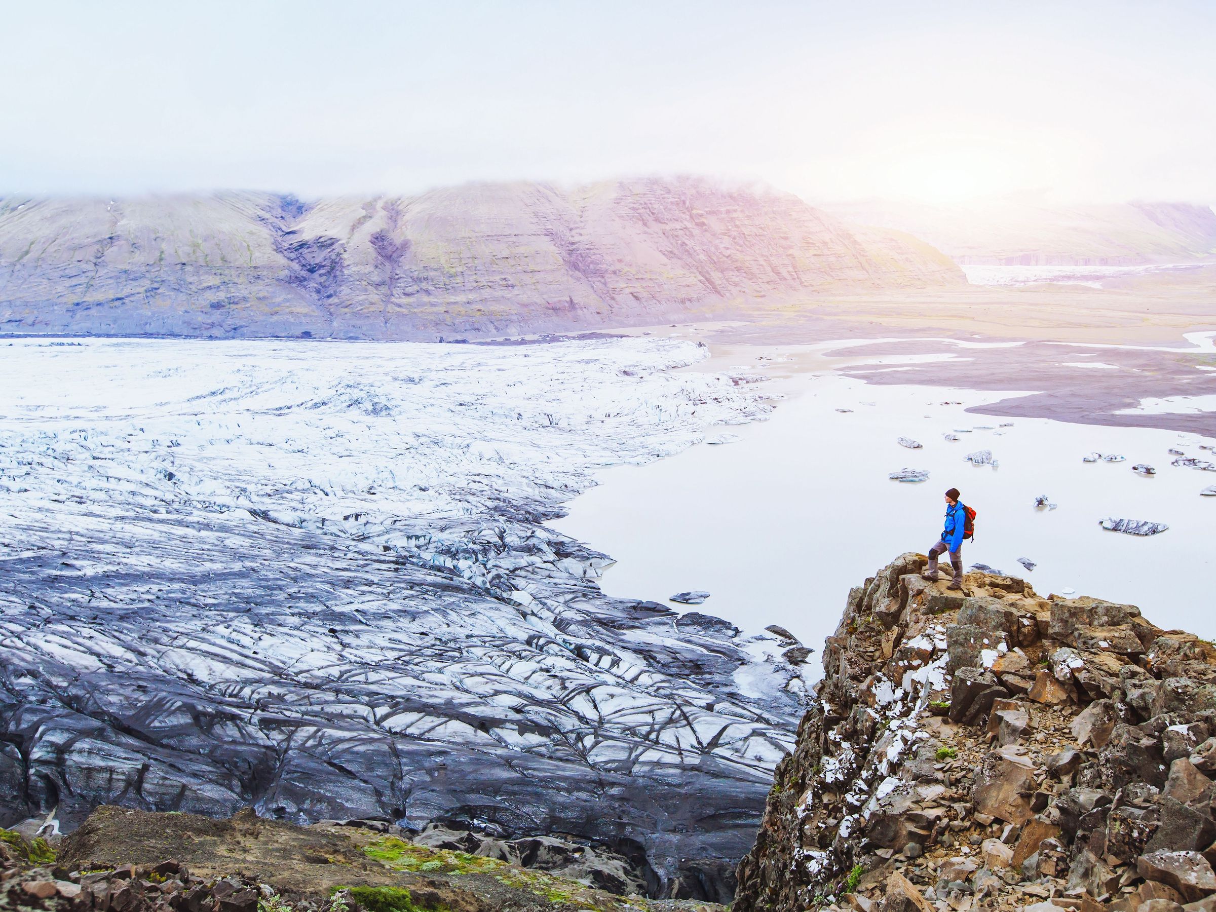 un hombre está de pie sobre un acantilado mirando un glaciar .