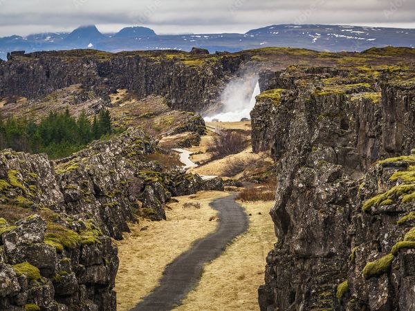 A winding path snakes through a moss-covered rift valley and leads to a distant waterfall.