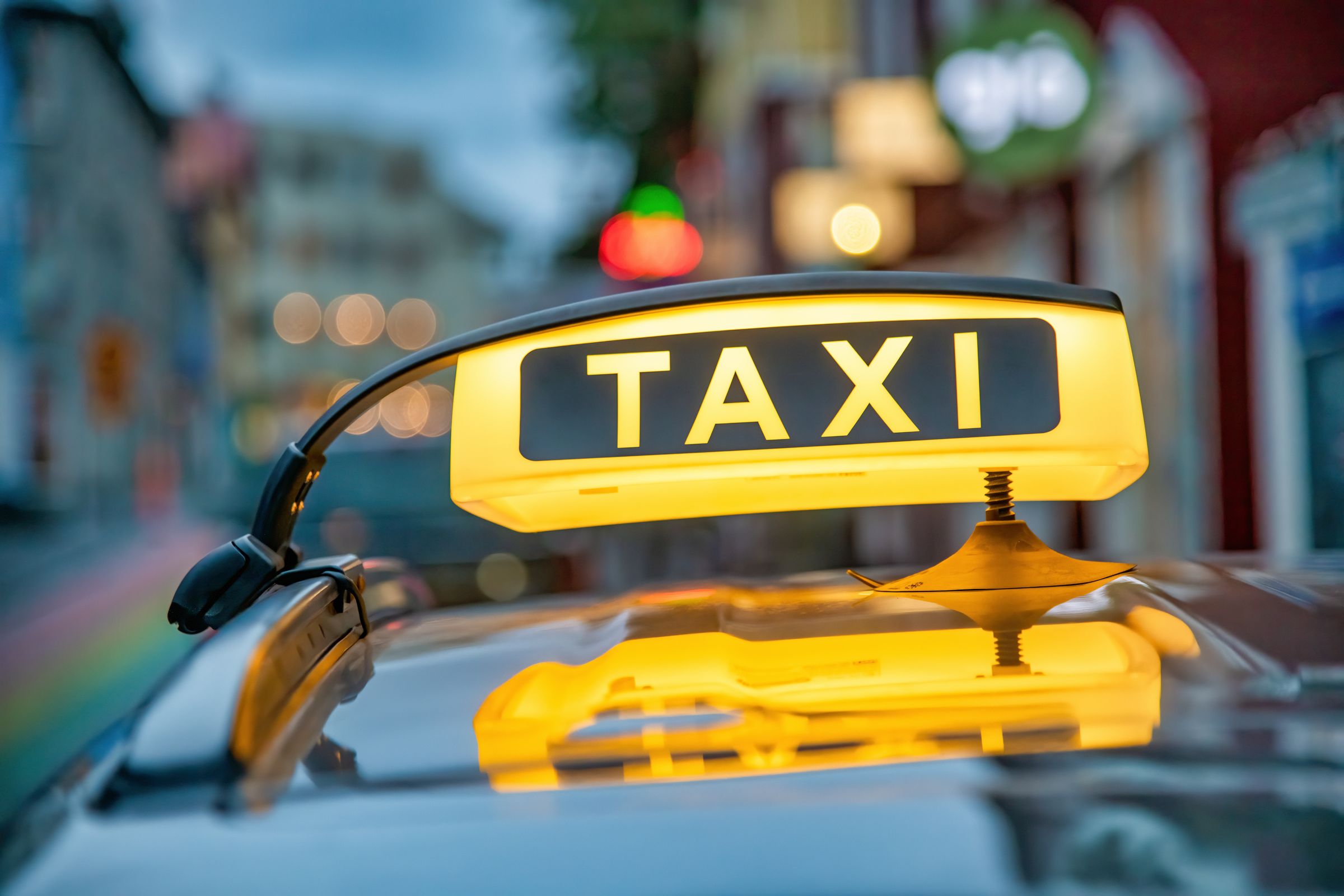 Un letrero amarillo brillante de "TAXI" sobre el techo de un coche, con la ciudad desenfocada de fondo.