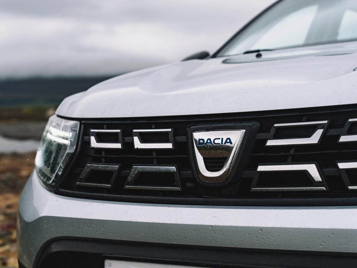 Primer plano de la parrilla del Dacia Duster Primer plano de la parrilla delantera y el emblema de Dacia de un Dacia Duster, con la costa al fondo