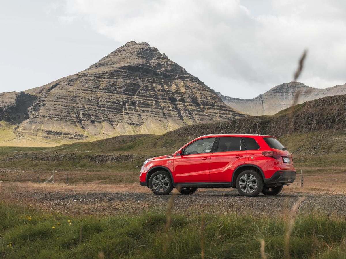 Champ de montagne Vitara Vue arrière d’un SUV Suzuki Vitara garé dans un champ, avec des montagnes en arrière-plan, location de SUV en Islande