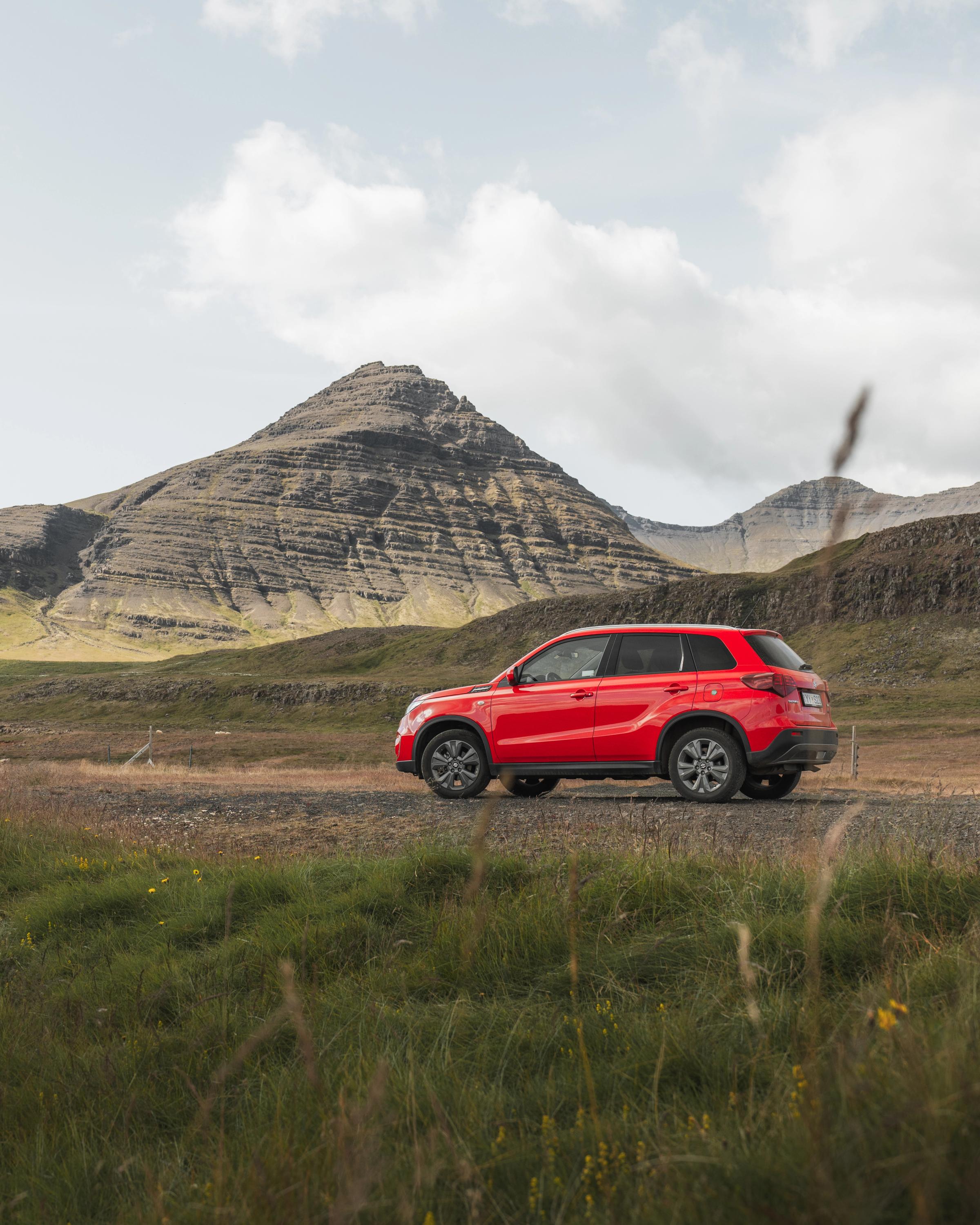 Champ de montagne Vitara Vue arrière d’un SUV Suzuki Vitara garé dans un champ, avec des montagnes en arrière-plan, location de SUV en Islande