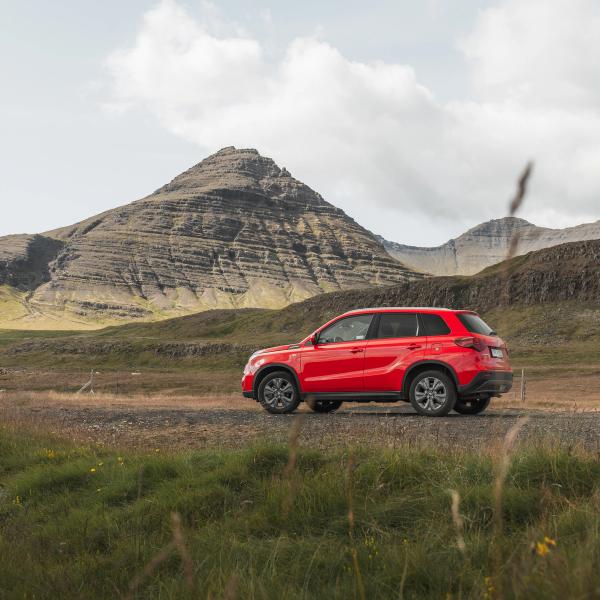 A red SUV on a dirt road in a mountainous, grassy landscape under a cloudy sky.