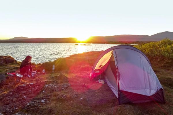 a person is sitting in front of a tent on the shore of a lake at sunset .
