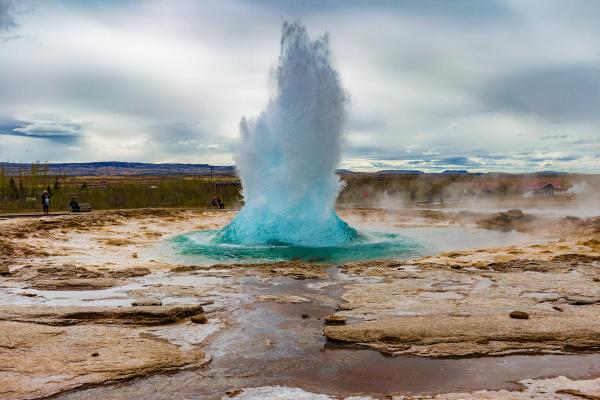 a blue geyser is erupting in the middle of a desert at Geysir in Iceland.