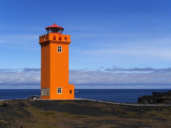 un faro naranja se encuentra en lo alto de una colina con vistas al océano .