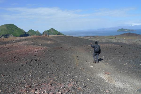 a man with a backpack is walking on a dirt path, Eldfell Volcano
